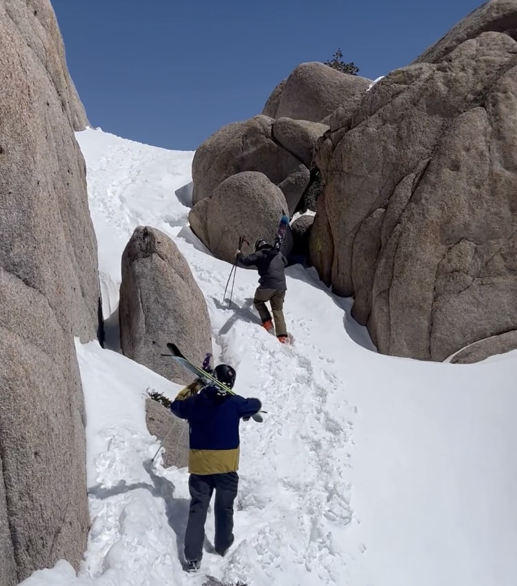 Two skiers hike through granite rocks on their way to ski.