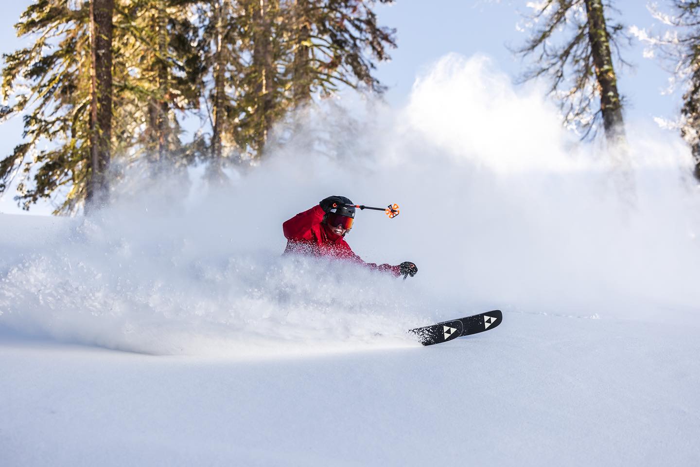 skier in deep powder on a snowy ski slope mountain with trees and blue sky in the background