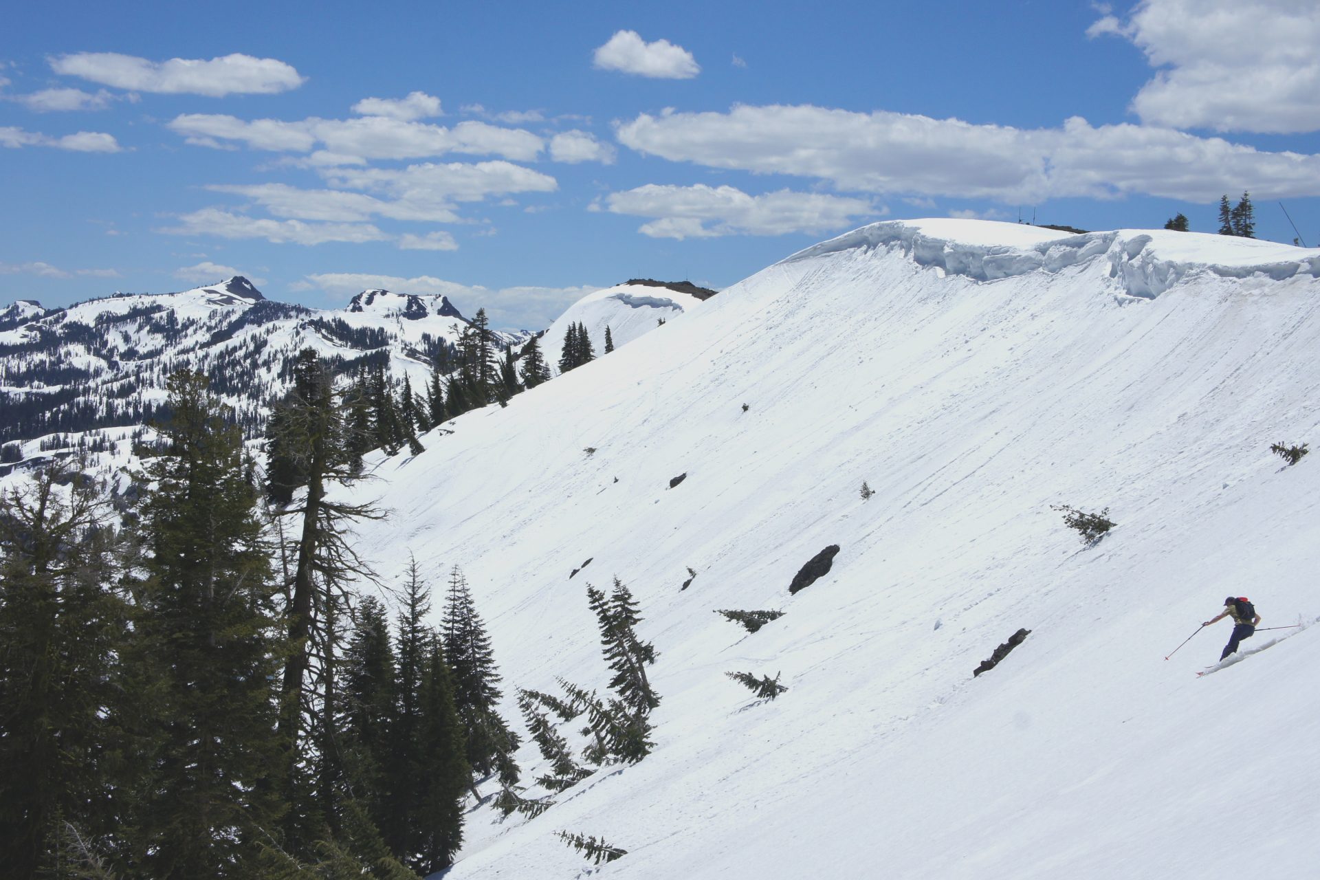 skier making a turn in a huge sunny bowl with large cornice overhead