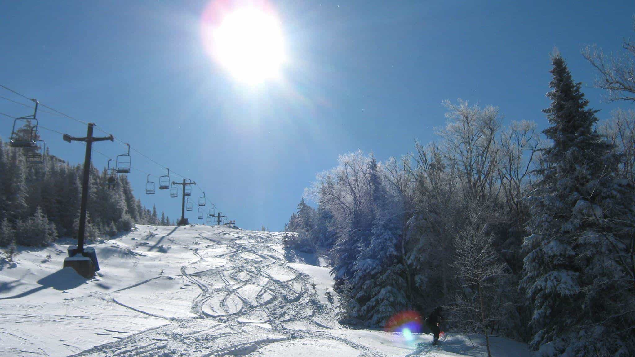 Powder day at big tupper resort with ski tracks in deep snow beneath chairlift while sun is shining in blue sky